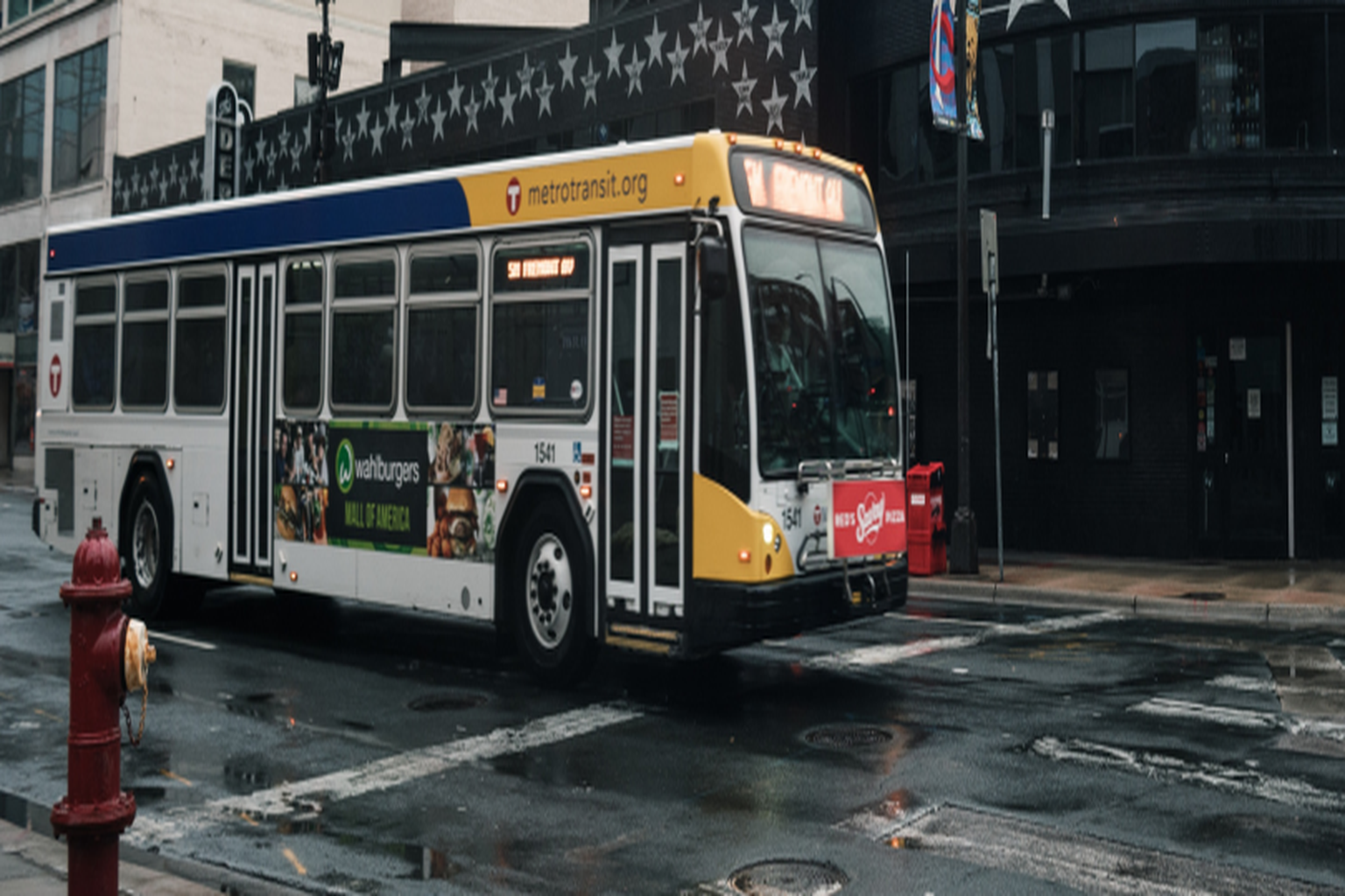 Metro Transit bus on wet city street with urban buildings in background